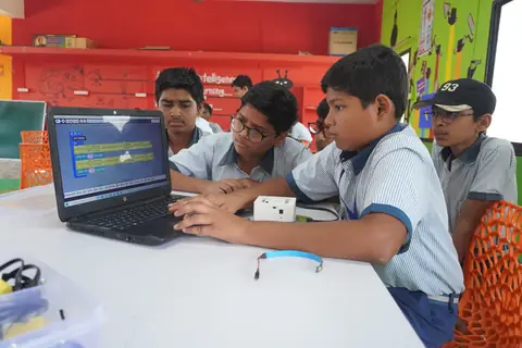 Students coding a microcontroller board on a laptop, with lab kits on the table