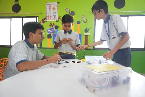 Three students wiring a circuit, kit box in front of them